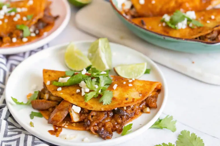 A plate of birria tacos with tender beef, cilantro, onion, and lime, topped with crumbled cheese.