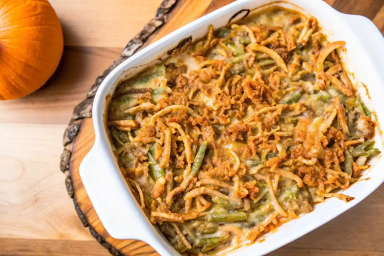 Green bean casserole with crispy fried onions, served in a white dish, with a pumpkin in the background.